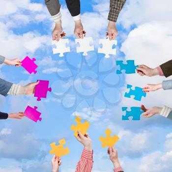 circle of people hands with different puzzle pieces with light blue sky and white clouds background