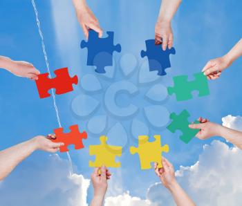 circle of people hands with different puzzle pieces with blue sky and rainbow background