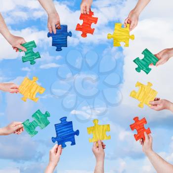 circle of people hands with painted puzzle pieces with blue sky and white clouds background