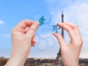male and female hands with little puzzle pieces with Paris district and Eiffel Tower background