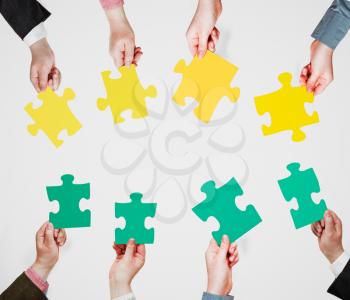 set of green and yellow puzzle pieces in opposite sides in people hands on grey background