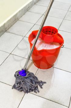 red bucket with washing water and mop the tile floors
