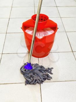 red bucket with foamy water and mop the tile floors