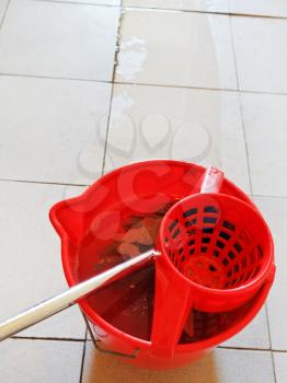 mop in red bucket with foamy water and washing the tile floor