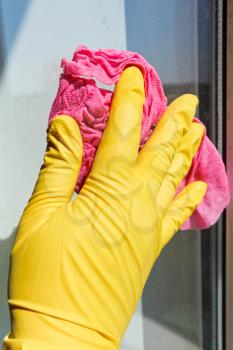 hand in yellow rubber glove washing window glass by wet cloth