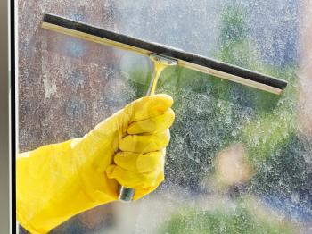 hand in yellow glove washes home window glass by squeegee in spring day