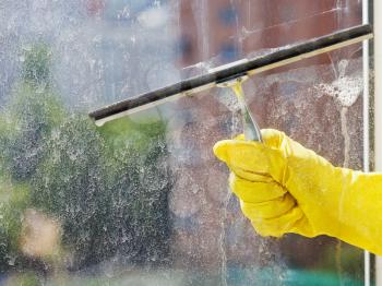 hand in yellow glove wiping home window glass by squeegee in spring day