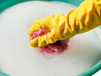 hand in yellow rubber glove rinsing wet cloth in foamy water