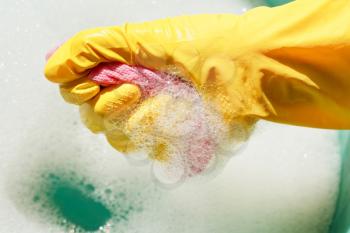 hand in yellow rubber glove wrings out wet duster from soapy water