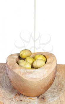 olive oil in thin stream flows on olives in wooden bowl close up isolated on white background