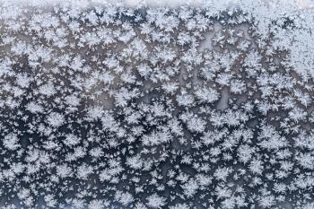snowflakes and frost on frozen windowpane in cold winter evening close up