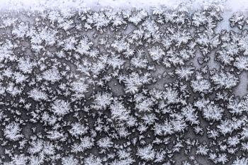 snowflakes and frost on frozen window pane in cold winter evening close up