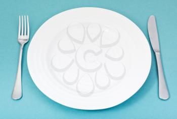 empty white plate with fork and knife set on green background