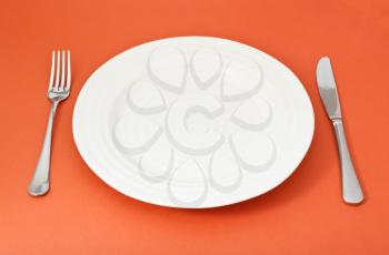empty white plate with fork and knife on red background