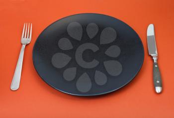 empty black plate with fork and knife on red background