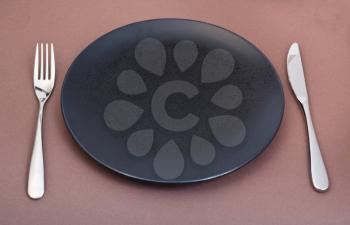 empty black plate with fork and knife set on brown background