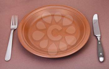 empty brown ceramic plate with fork and knife on brown background