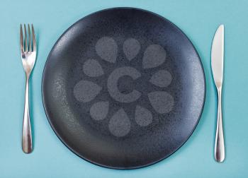 top view of empty black plate with fork and knife set on green background