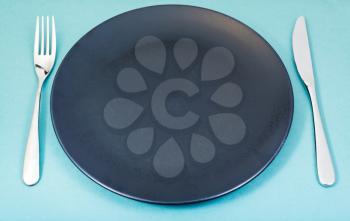 empty black plate with fork and knife set on green background