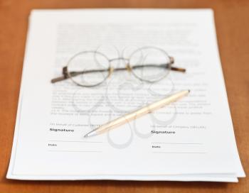 pages of sales contract, golden pen and eyeglasses on wooden table
