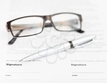 silver pen and eyeglasses on signature page of sales contract