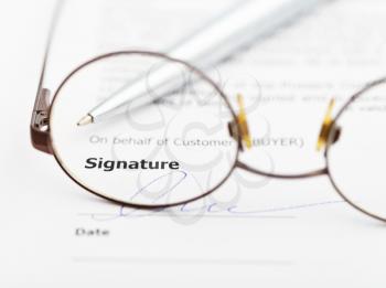 signature of sales agreement and silver pen through eyeglasses