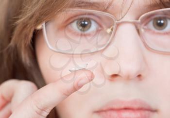 girl with glasses holds contact lens on your finger near the eyes