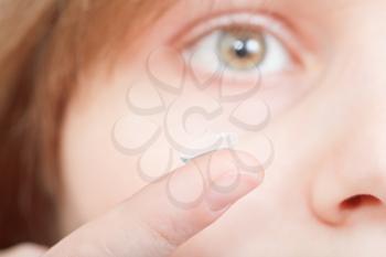 finger with corrective lens in front of female face close up