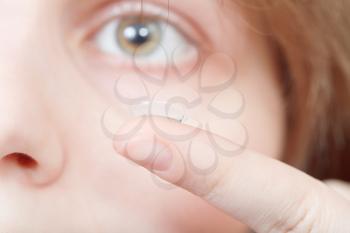 finger with contact lens near woman's face close up