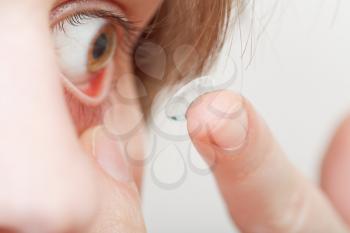 young woman inserting contact lens in eye close up