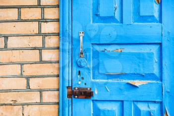 details of closed shabby blue wooden door in brick wall