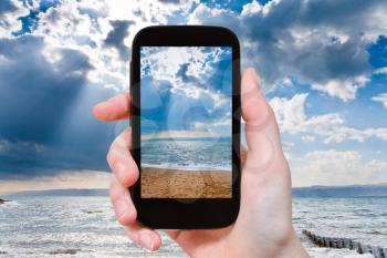 travel concept - tourist taking photo of sunbeams over Dead Sea on mobile gadget, Jordan