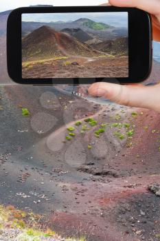 travel concept - tourist taking photo of path on slope of craters volcano Etna on mobile gadget, Sicily, Italy