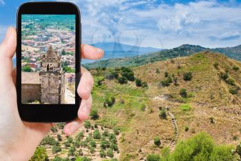travel concept - tourist taking photo of calatabiano town on Etna slope on mobile gadget, Sicily, Italy