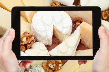 photographing food concept - tourist taking photo of assortment of cheeses on wooden plate on mobile gadget, France