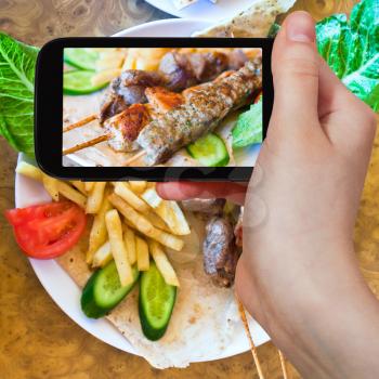 photographing food concept - tourist taking photo of skewers mix arabic kebabs on mobile gadget, Jordan