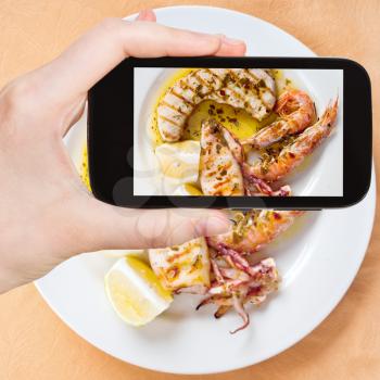 photographing food concept - tourist taking photo of sicilian grilled fish mix on white plate on mobile gadget, Sicily, Italy