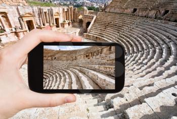 travel concept - tourist taking photo of arena in Large South Theatre in ancient town Jerash in Jordan on mobile gadget