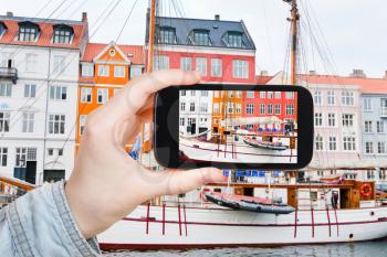 travel concept - tourist taking photo of Nyhavn waterfront, canal and entertainment district in Copenhagen on mobile gadget, Denmark
