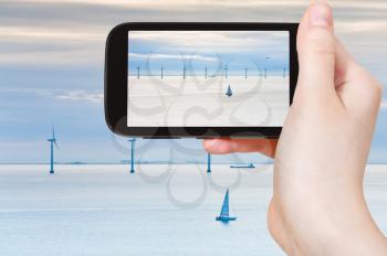 travel concept - tourist taking photo of Middelgrunden - offshore wind farm near Copenhagen, Denmark at early morning on mobile gadget