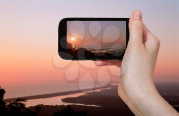 travel concept - tourist taking photo of salt Lakes at pink sunset near Sabaudia town on mobile gadget, Italy