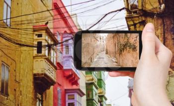 travel concept - tourist taking photo of medieval narrow street in Valletta on mobile gadget, Malta