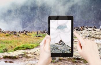 travel concept - tourist taking photo of stone pyramid on mountain plateau in Norway on mobile gadget