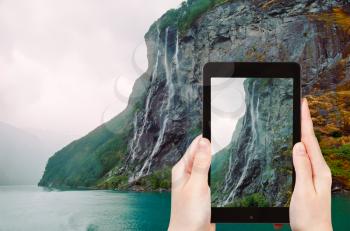 travel concept - tourist taking photo of seven sisters waterfall over Geirangerfjord on mobile gadget