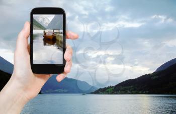 travel concept - tourist taking photo of fjord in Norway in evening on mobile gadget