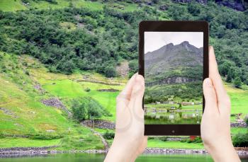 travel concept - tourist taking photo of village in Norway on coast of fiord on mobile gadget