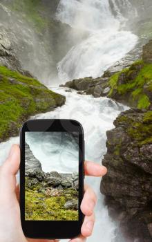 travel concept - tourist taking photo of kjosfossen waterfall in Norway on mobile gadget