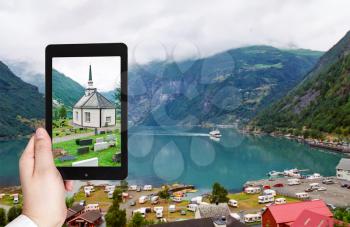 travel concept - tourist taking photo of geiranger village on beach of geirangerfjord fjord in Norway on mobile gadget
