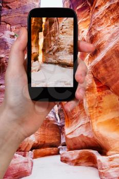 travel concept - tourist taking photo of The Siq - narrow gorge to ancient city Petra, Jordan on mobile gadget