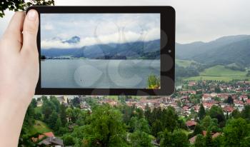 travel concept - tourist taking photo of Schliersee town - climatic health resort in Bavarian Alps on mobile gadget, Germany